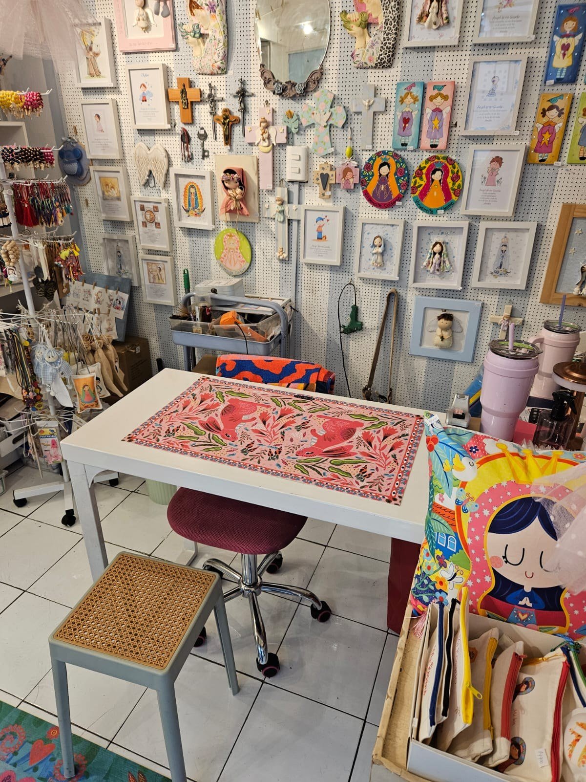 Mesa de trabajo de Hada Mágica junto a la pared de estampas, cruces y santitos personalizados